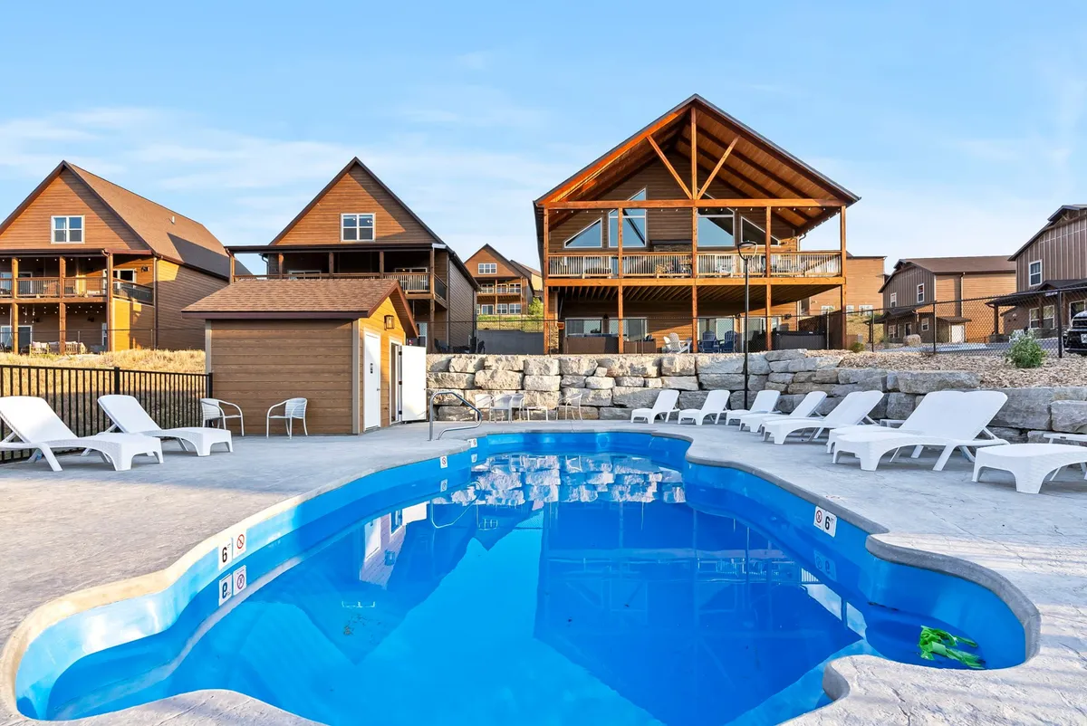 An inviting pool area set against the backdrop of wooden cabins, with lounge chairs arranged around the water. The scene exudes a relaxed, cheerful mood, perfect for swimming, sunbathing, and social gatherings. The sunset casts a warm glow, and the amenities suggest both quiet mornings by the pool and lively evening barbecues.