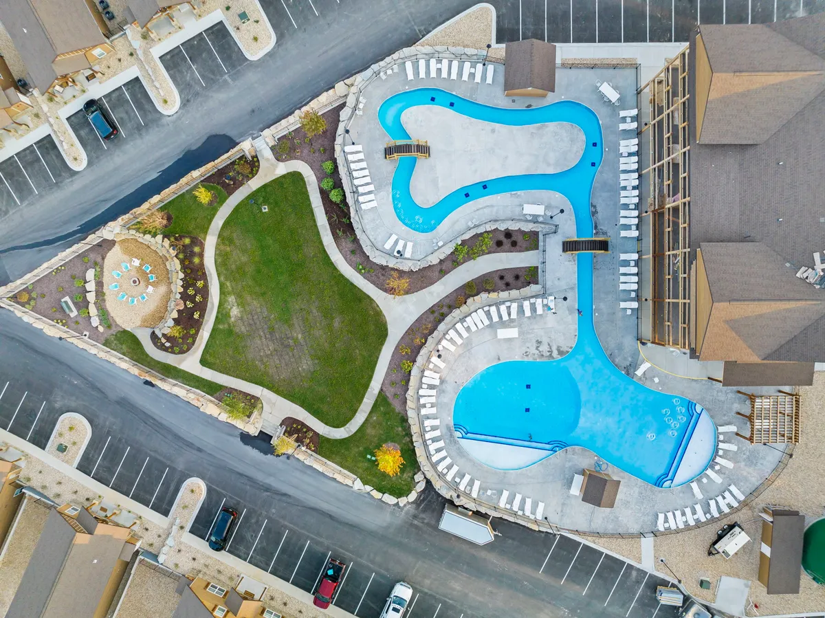 A lively pool area with multiple swimming pools, surrounded by landscaped gardens, lounge chairs, and a seating area with tables. The vibe is relaxed and cheerful, ideal for both daytime fun and evening social gatherings around the fire pit.