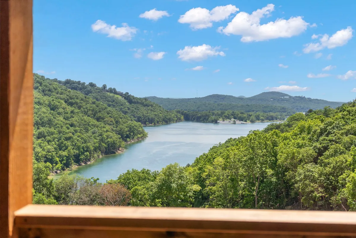 The image captures a serene view of Table Rock Lake, bordered by lush green trees and gentle rolling hills under a bright blue sky dotted with puffy clouds. The expansive lake invites activities like boating and fishing, while the natural surroundings evoke a sense of peace and relaxation.