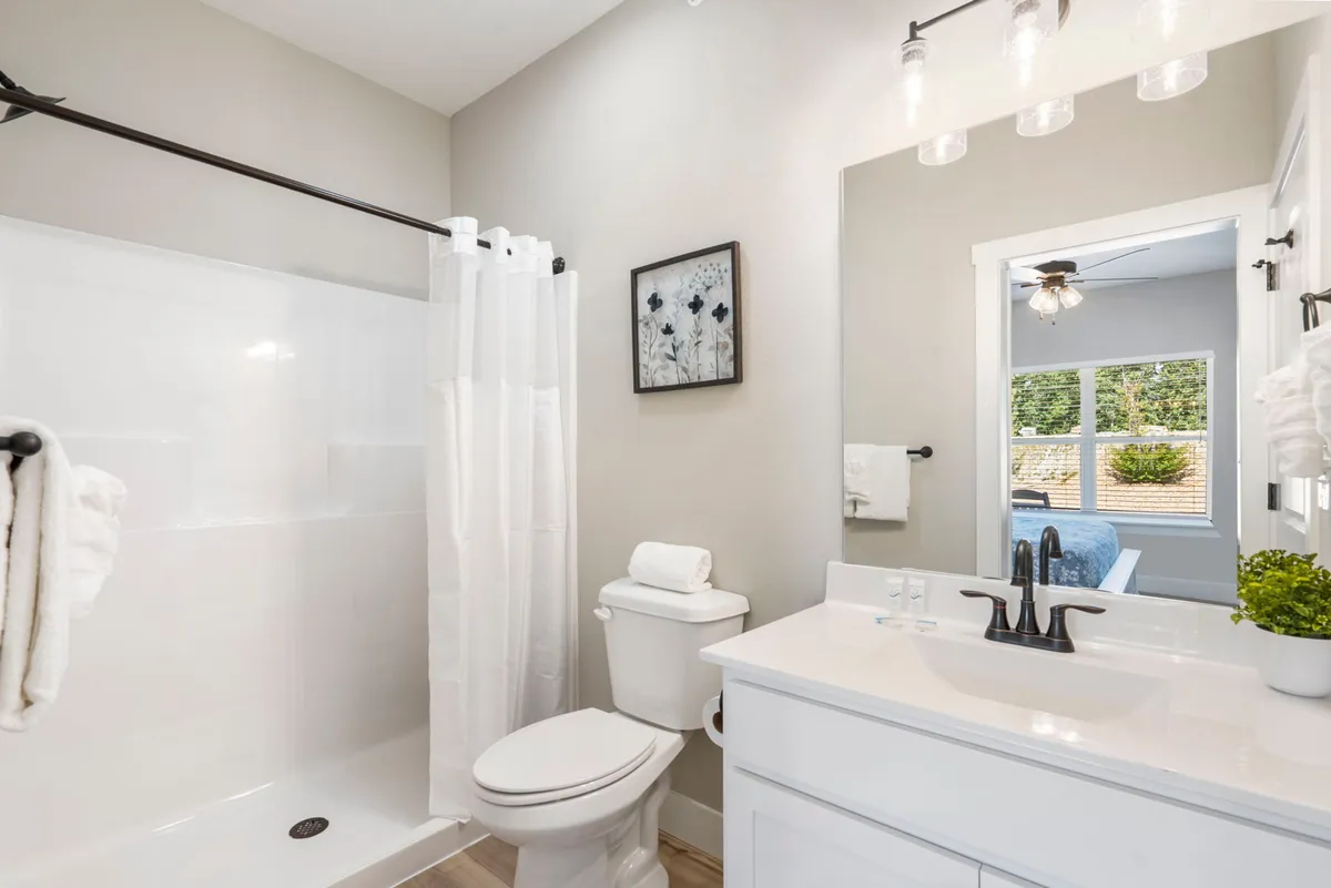 A modern, calm bathroom with a spacious shower, vanity with a sink, toilet, and wall art. The space is bright and peaceful, reflecting a setting for personal comfort and refreshment.