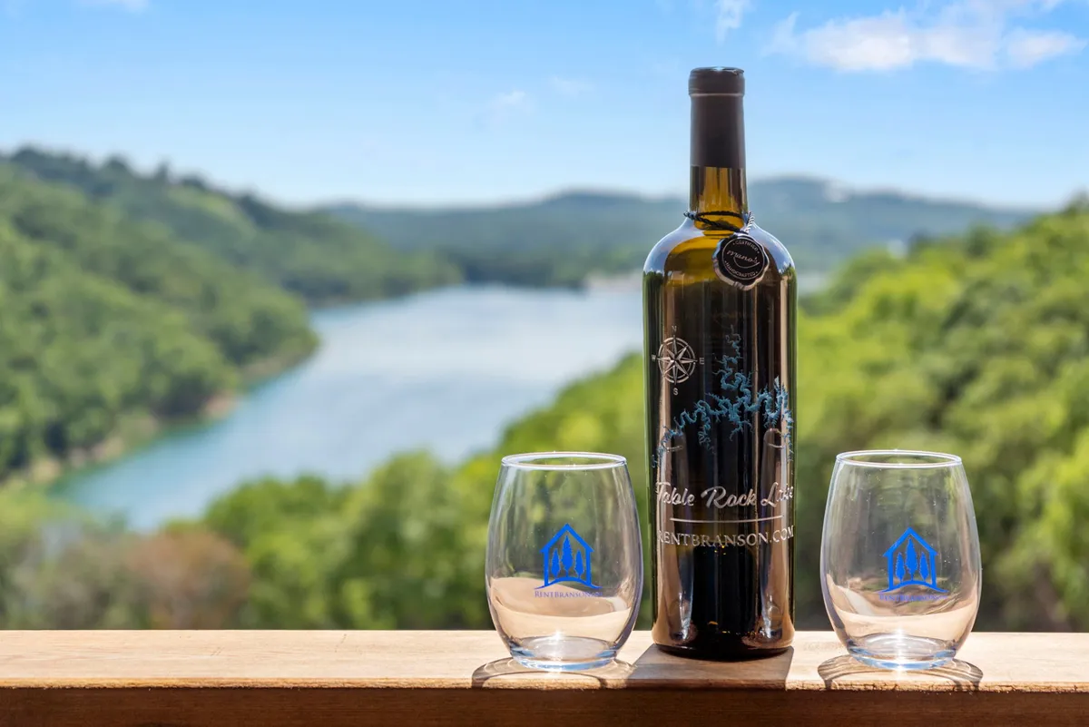 A tranquil lakeside setting with a wine bottle and two glasses set out, offering a scenic view of the lake. The mood is peaceful and intimate—perfect for enjoying drinks at sunset with friends or a partner.