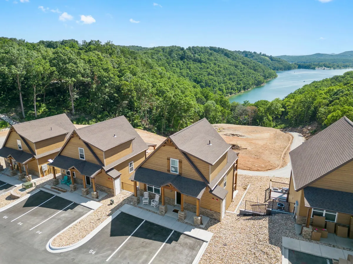 This image captures a cluster of wooden cabins nestled along the shoreline of a lake, with lush greenery surrounding the area. The tranquil water and nearby trees evoke an inviting sense of natural escape, making it clear this is a place where guests can step right into nature for lakeside relaxation, hiking, or community gatherings.