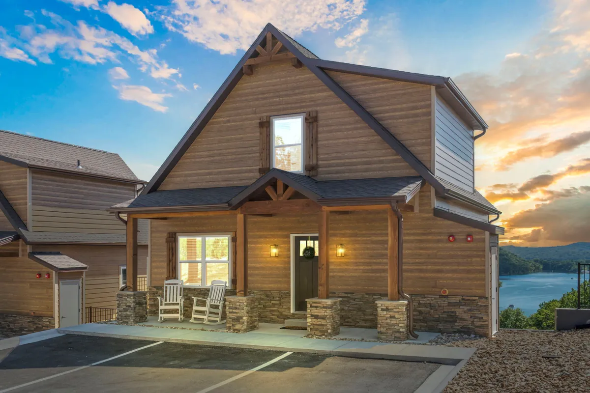 The front porch of a rustic cabin with rocking chairs, a stone foundation, large windows, and sweeping views of the lake. The inviting setup encourages guests to relax after a day of adventure and enjoy sunsets or early morning coffee with nature as their backdrop.