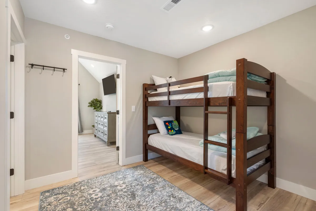 A playful bedroom with a twin over twin bunk bed, a cozy area rug, and a decorative pillow. The decor suggests a space designed with children in mind, offering both fun and comfort for younger guests.