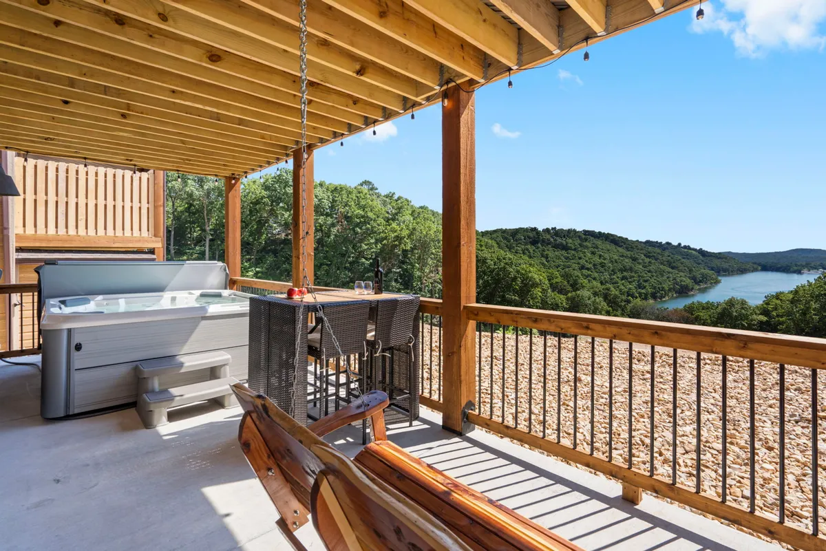 A serene lakeside hot tub adjacent to a bar area, with panoramic views of the water. The scene invites guests to unwind in the hot tub while soaking in the lake vistas, perfect for peaceful evenings or social gatherings under string lights.