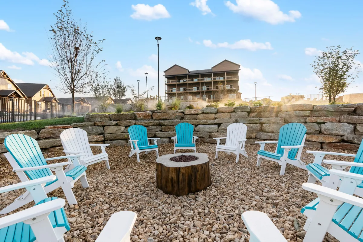 A cozy, communal fire pit encircled by Adirondack chairs, set against a natural stone wall and surrounded by trees. The setting is perfect for evening gatherings, storytelling, and roasting s’mores under the stars.