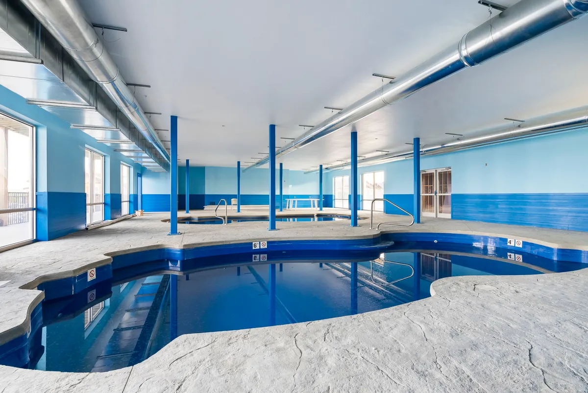 A peaceful indoor swimming pool surrounded by blue walls and large windows, letting in natural light. The tranquil setting invites guests to swim or relax regardless of the weather, ensuring year-round enjoyment.