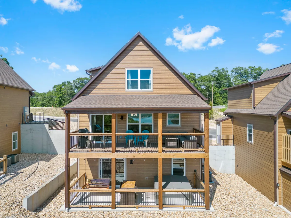 A wooden deck furnished with blue outdoor chairs overlooks lush greenery and features large windows leading inside. The atmosphere is relaxed and welcoming, ideal for sunset views, outdoor dining, or evening gatherings with friends and loved ones.